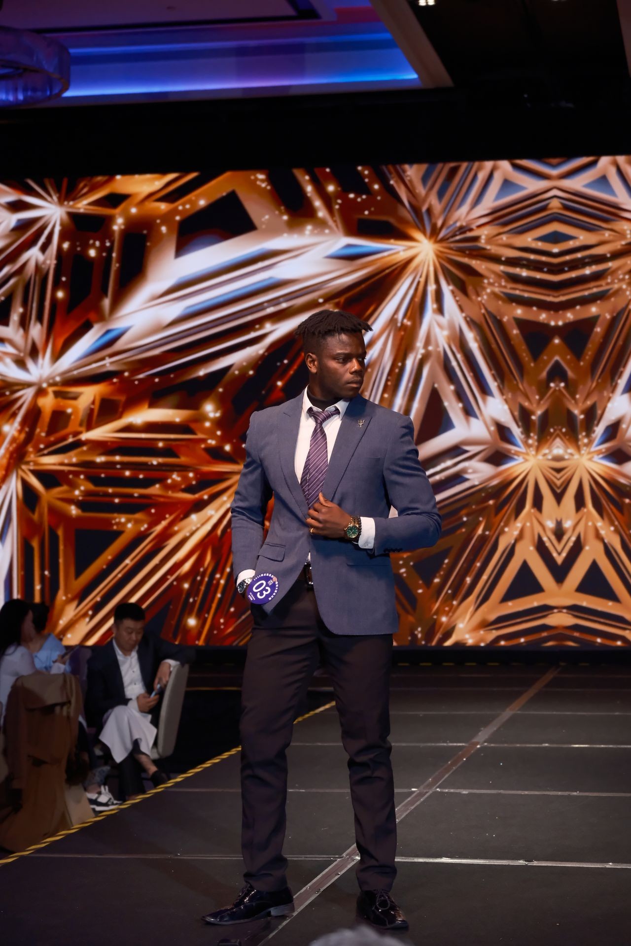 Person in a suit walking on a runway with an abstract geometric background display.