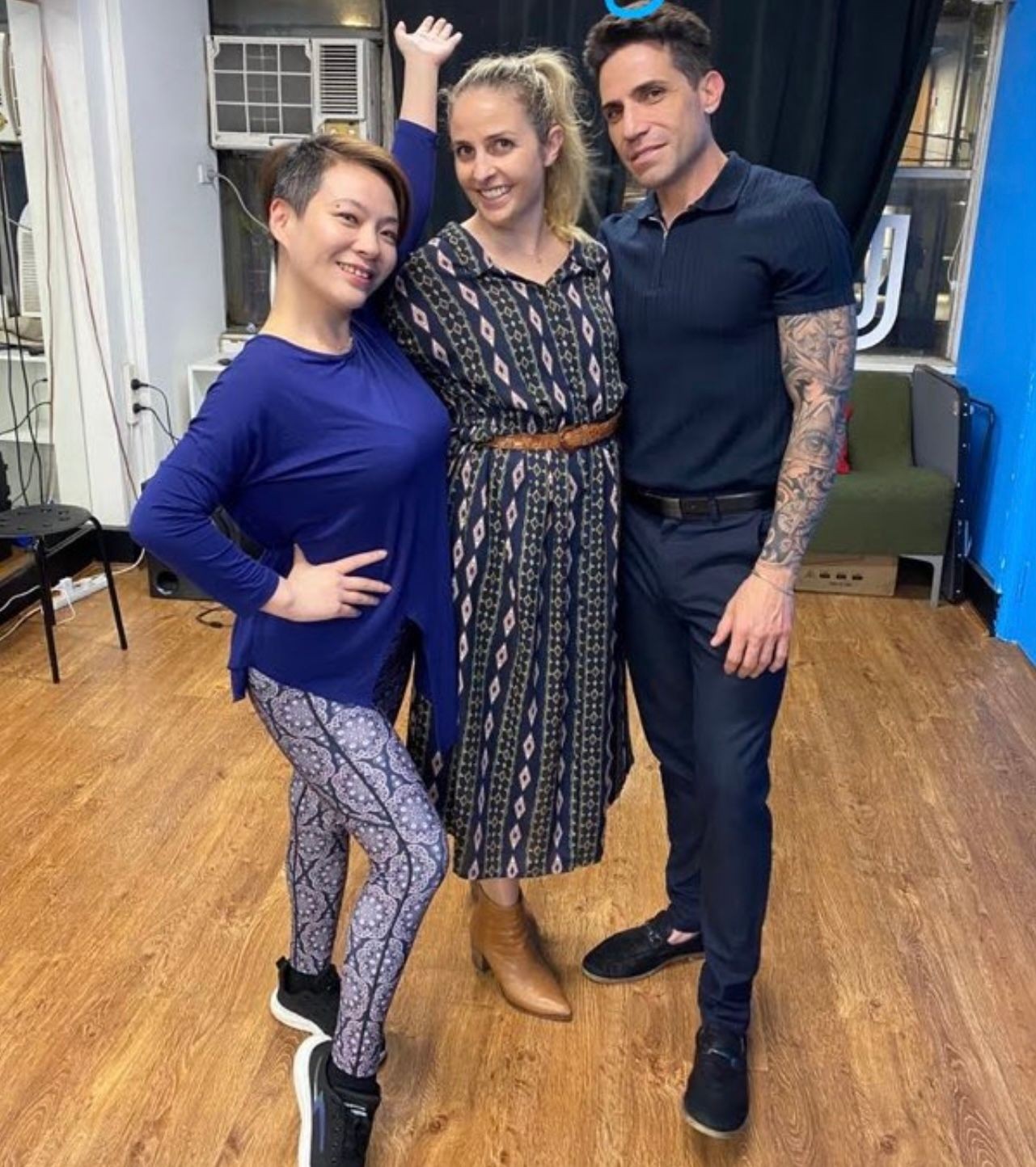 Three people posing happily in a room with wooden flooring and air conditioning units on the wall.